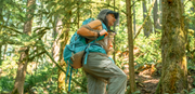young woman hiking through the forest wearing a bug jacket, bug pants, and a blue backpack