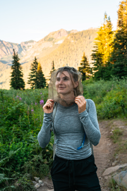 Young woman wearing a mesh bug head-net and hiking through the mountains at sunset