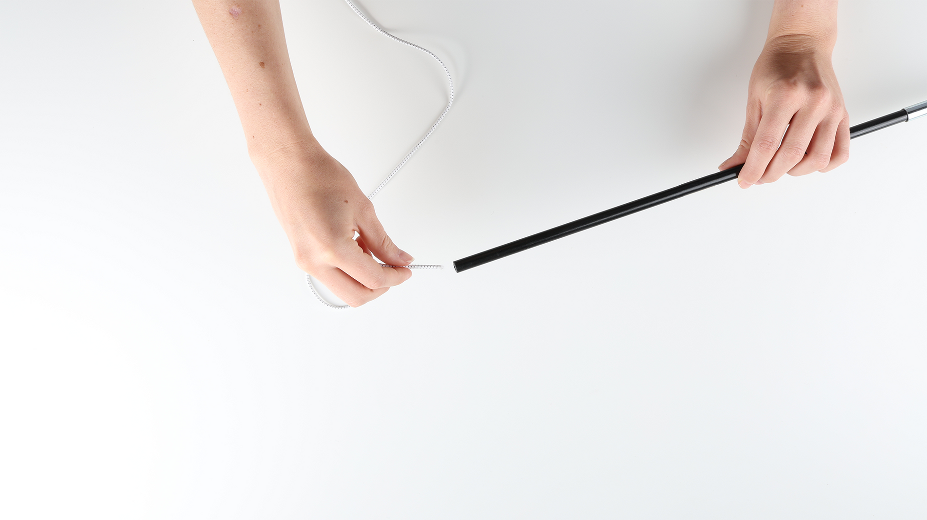 A person on one hand holding a shock cord and about to thread it through the tip of section of a tentpole that they are holding on the other hand