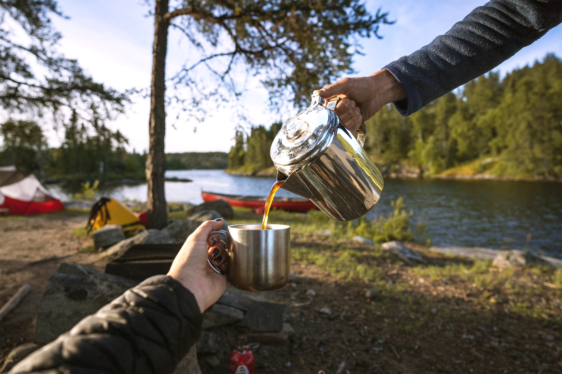 Person pours fresh coffee from a percolator into a lightweight mug at a campsite