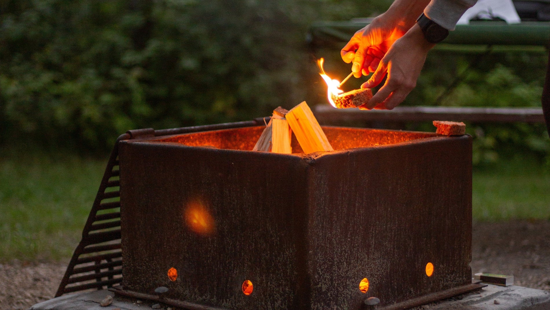 Hands lighting a fire starter using a match at a campsite fire-pit