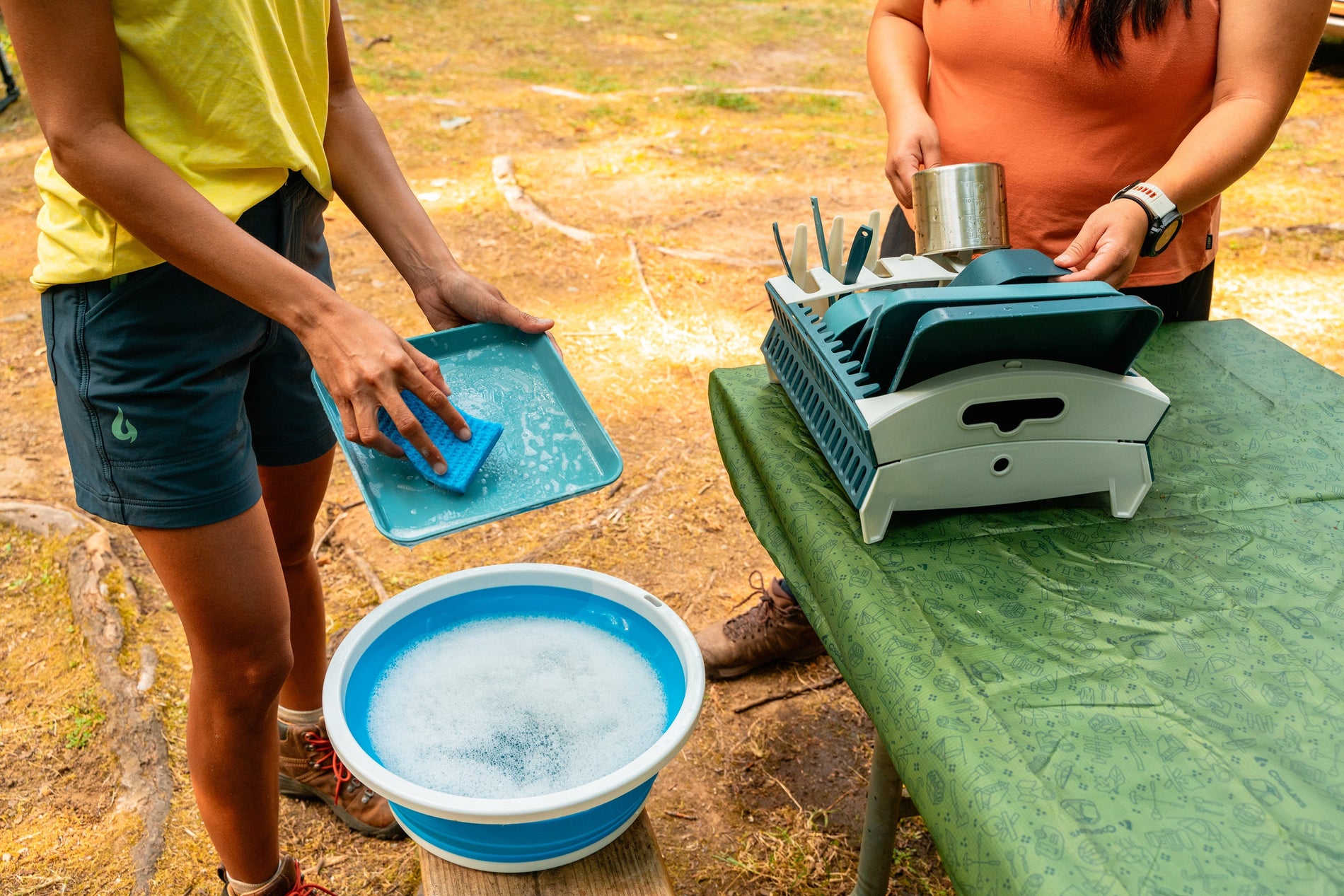 Lower body view of two people standing while washing and drying dishes at a campsite