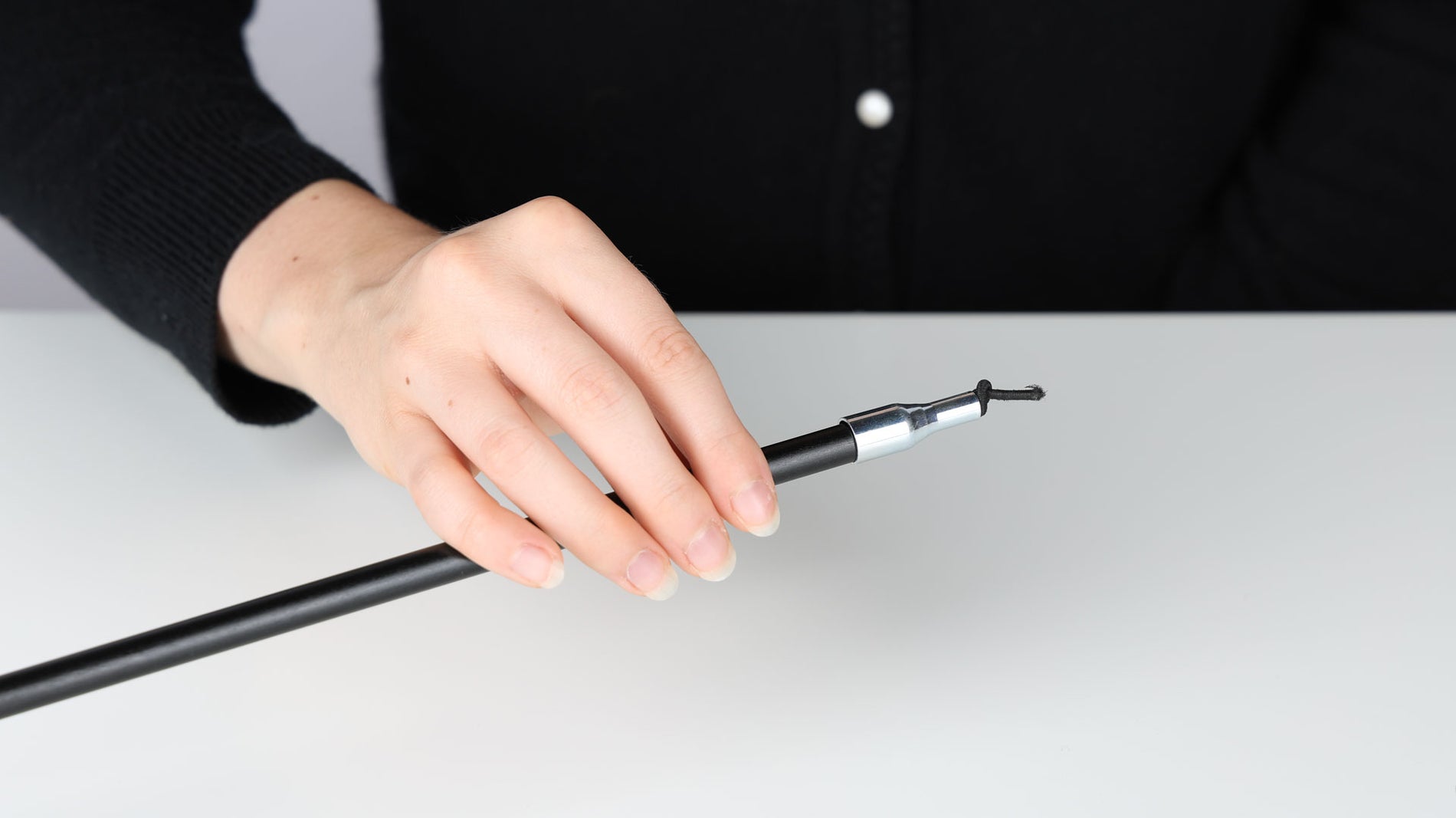 An image of a hand holding a Coghlan's replacement tent pole with a silver metal end cap. The shock cord is visible and is tied as it comes out of the metal end cap.