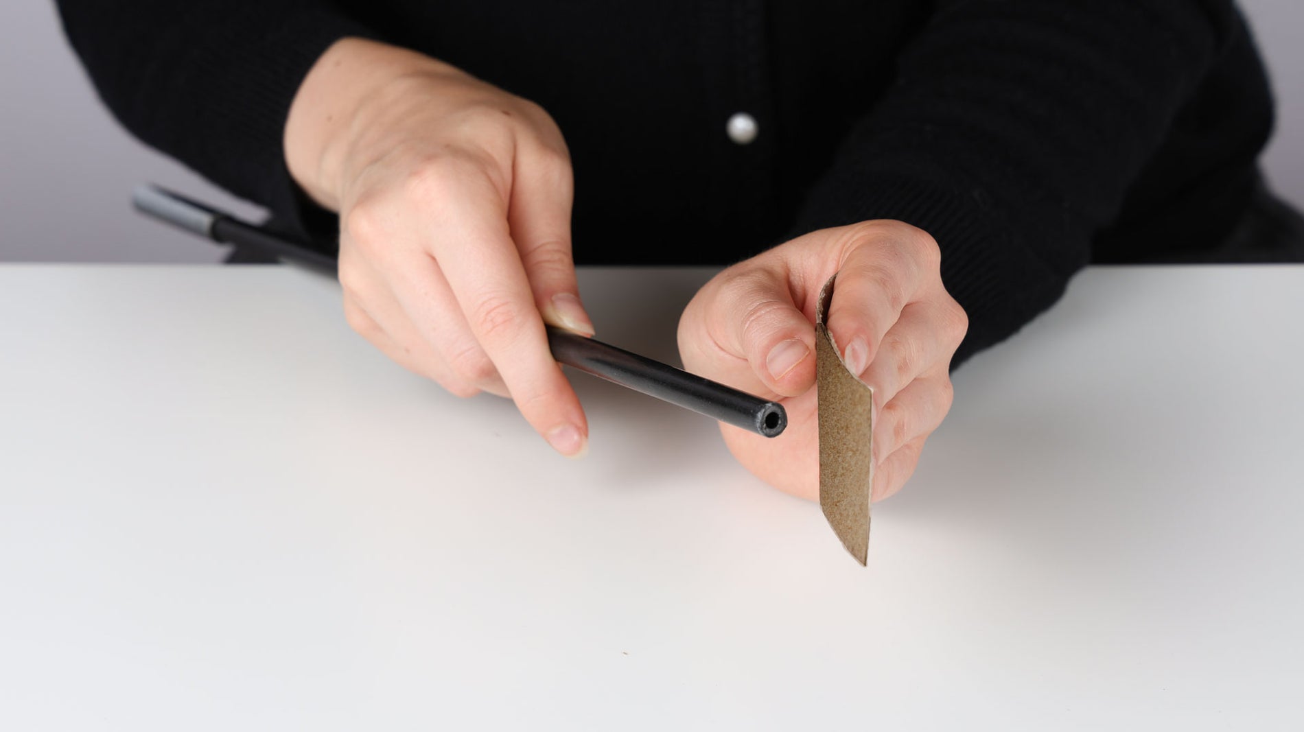 In one hand is a cut tent pole, and in the other hand is a piece of sandpaper, used to smooth out the rough cut end.