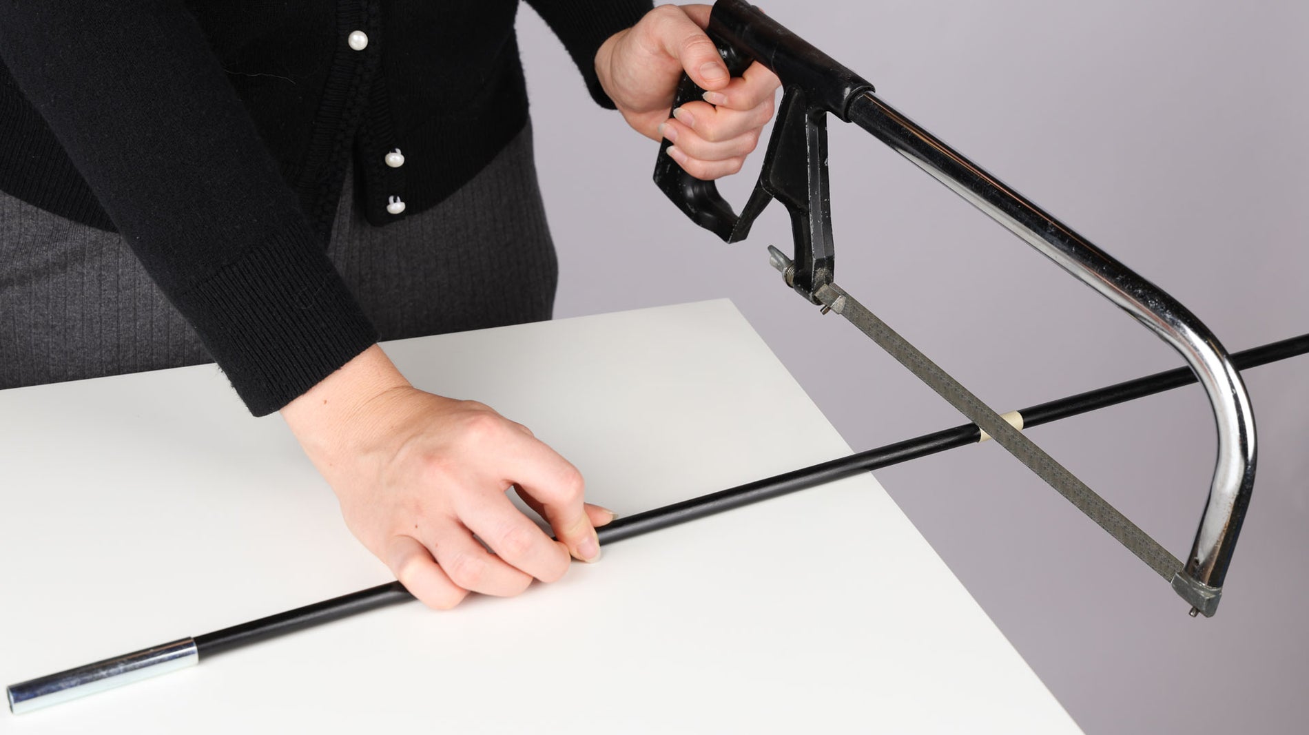 A person is at a table, showing hands holding a saw that is about to cut a Coghlan's replacement tent pole in order to shorten it.