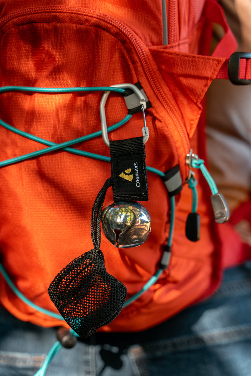 Metal bear bell attached to a carabiner hanging from the back of an orange hiking backpack