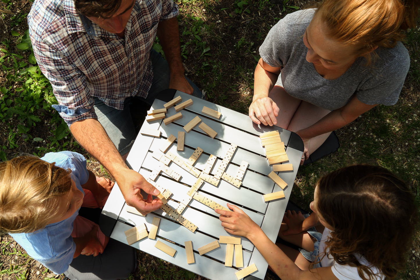 Overhead image of a family of four playing a domino game using the wood bricks outdoors