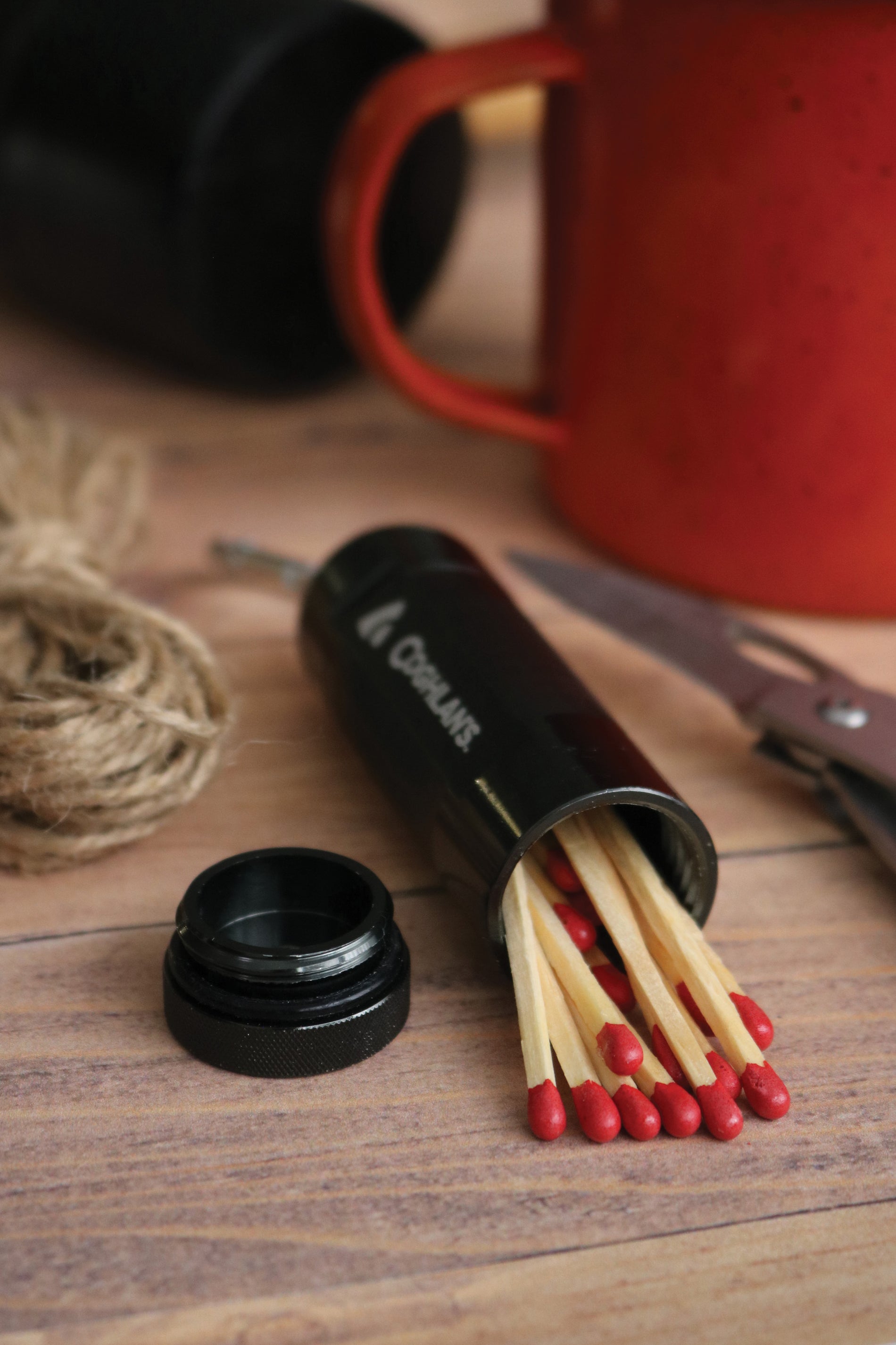 Close up view of an open match case exposing matches surrounded by other tools on a wooden table