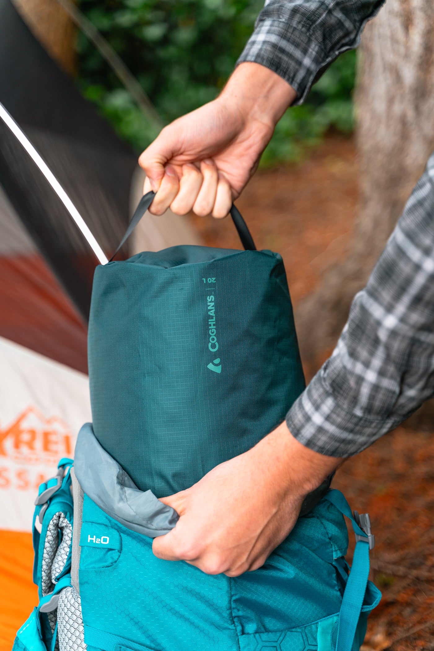 Teal dry bag being pulled by a handle out of a blue hiking backpack at a campsite