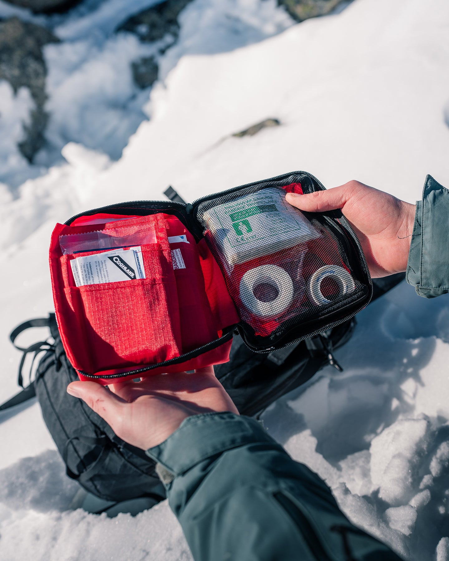 Person holding an open-faced first aid kit with tape and bandages over a snowbank.