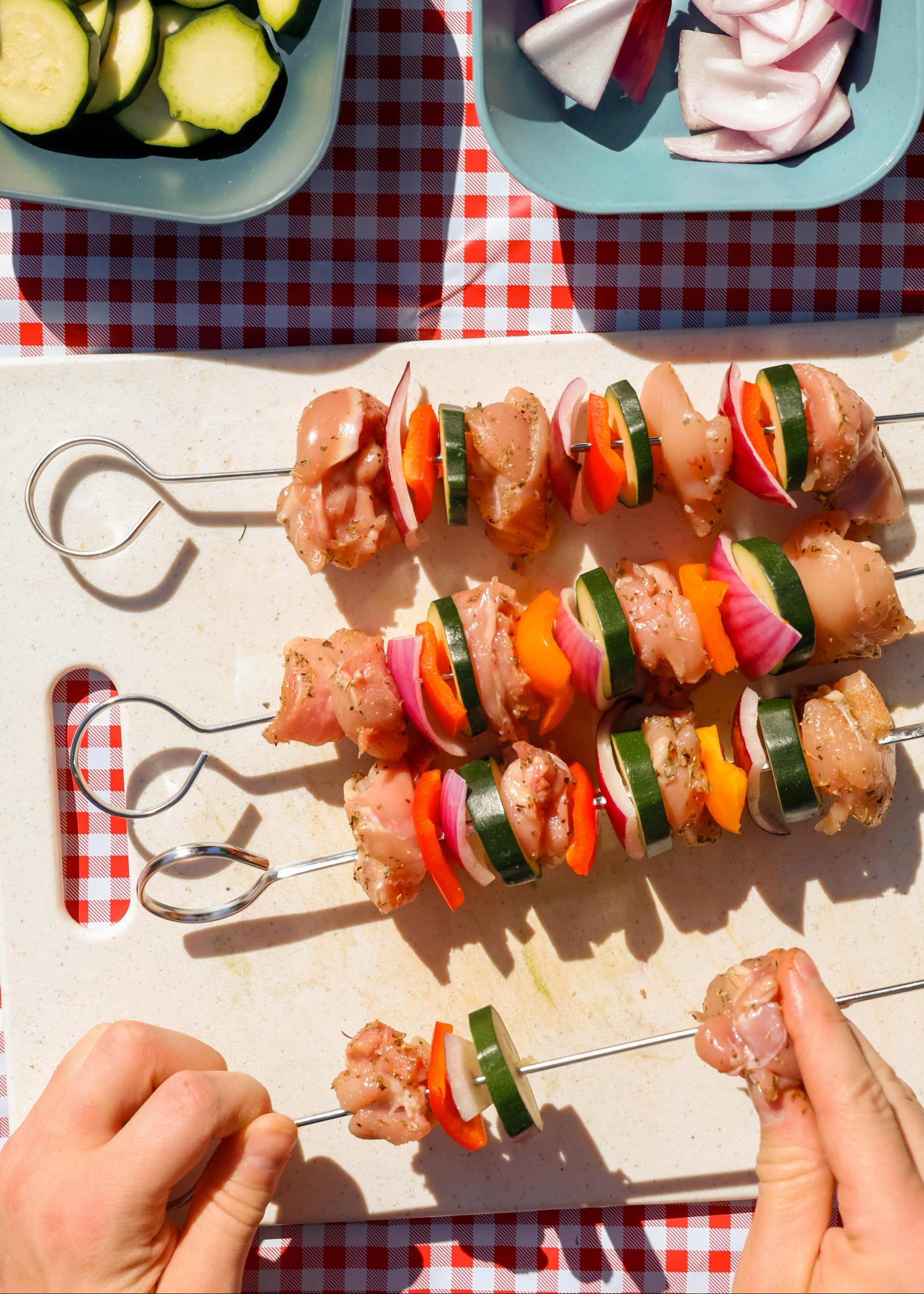Close-up of person's hands assembling chicken and veggie skewers over a cutting board