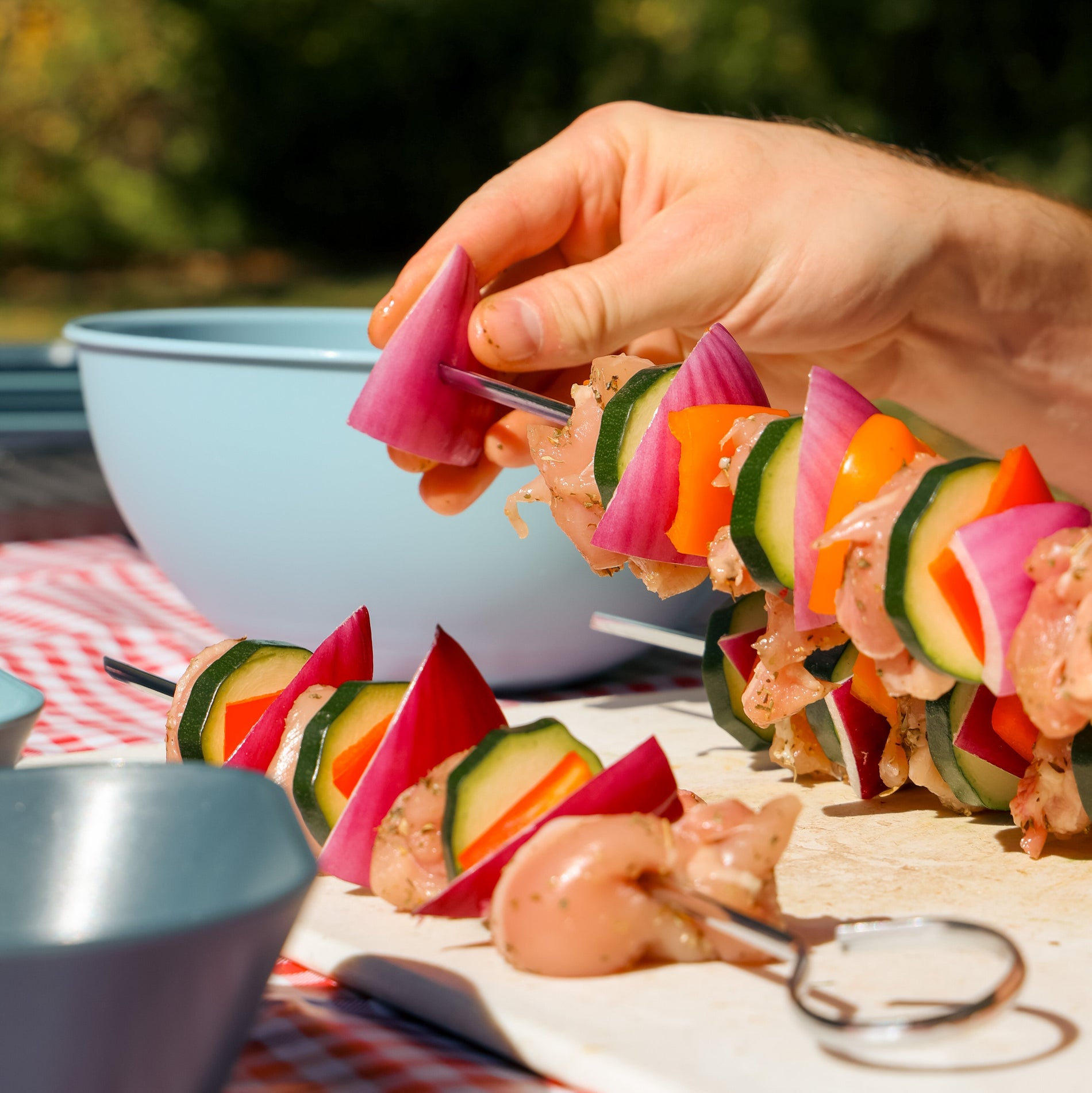 Hands sliding a piece red onion onto a metal skewer to make kebabs at a campsite