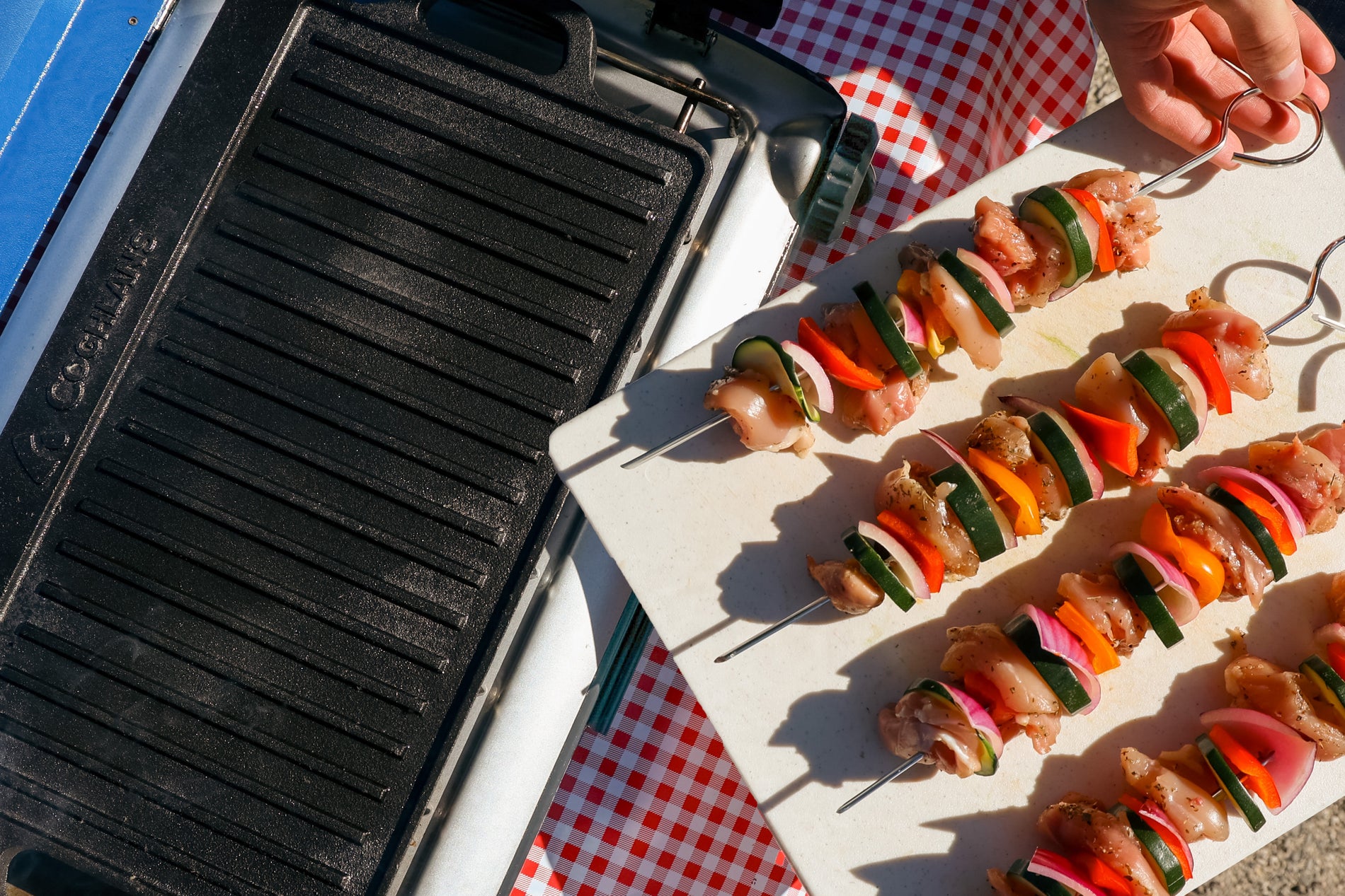 Chicken skewers on a white cutting board about to be placed on a cast iron griddle on a portable stove