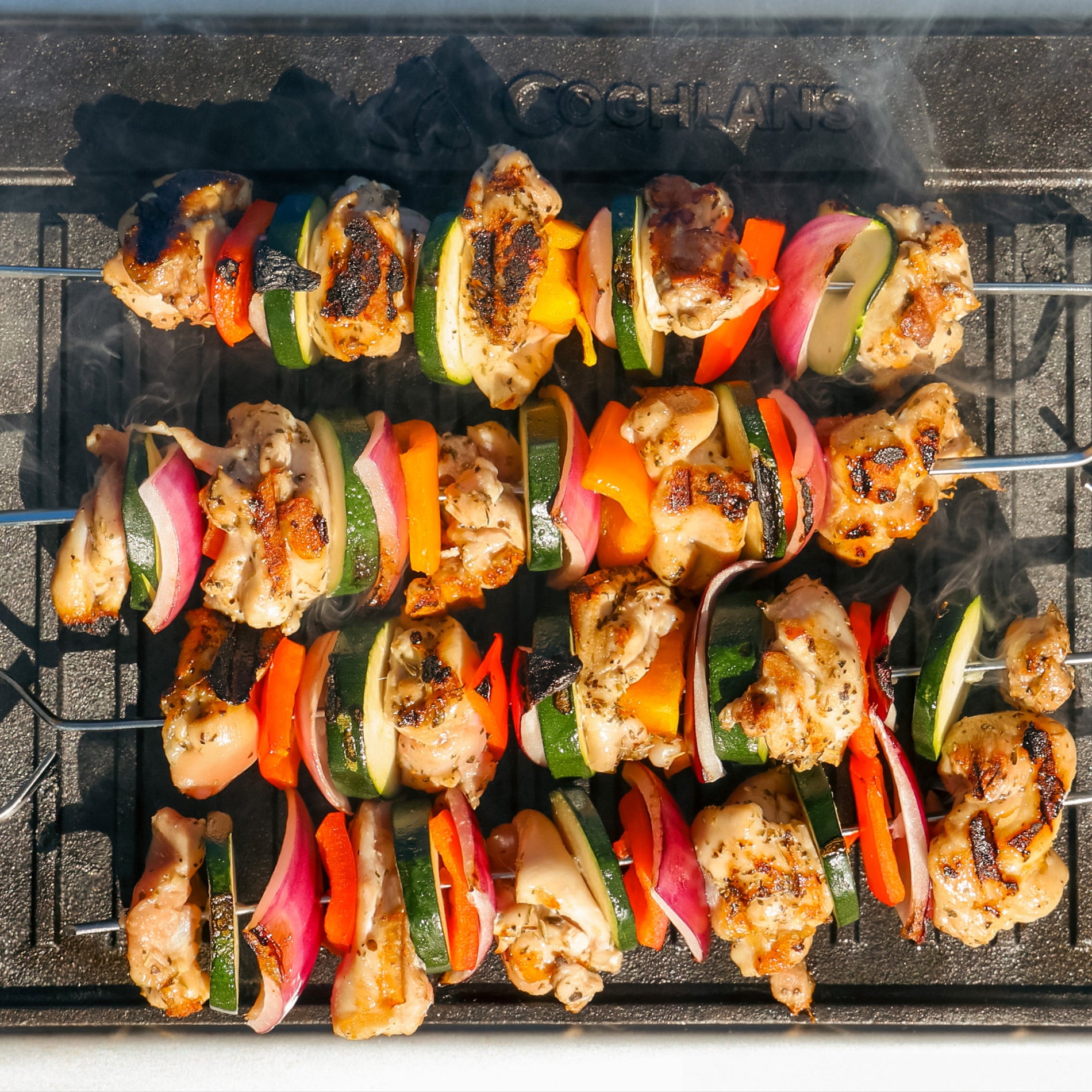 Close-up of chicken and vegetable kebabs with char marks being grilled on a cast iron griddle