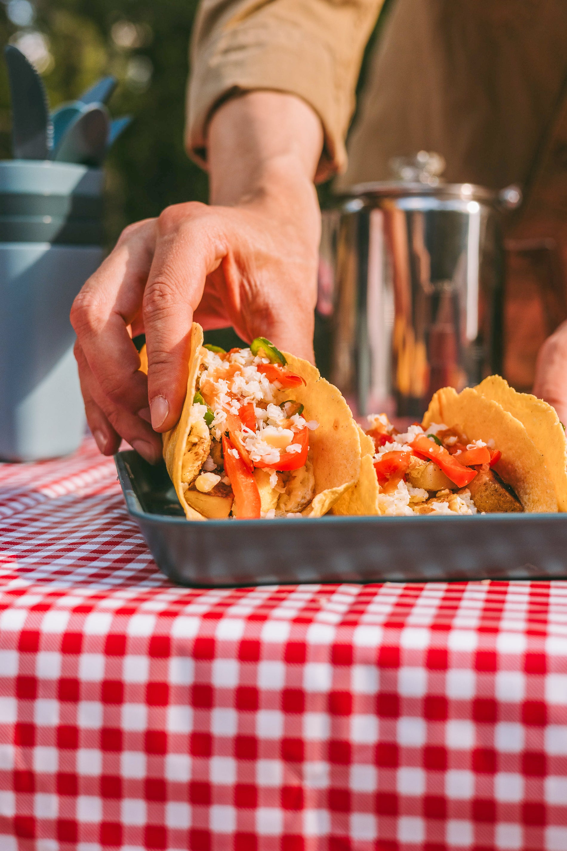 Three breakfast tacos on a Coghlans plate with a person's hand about to pick up a taco