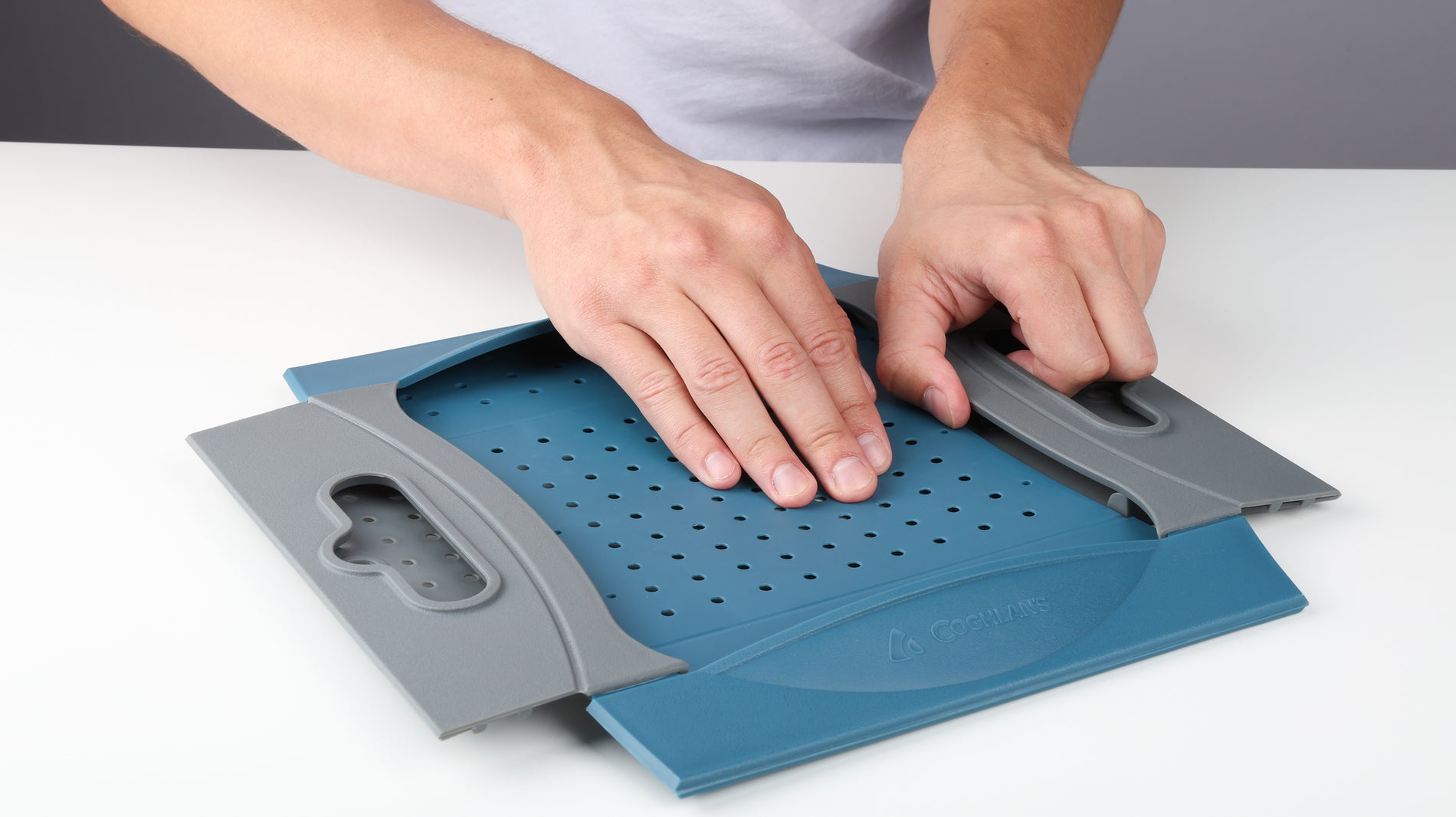 Hands pressing down and about to unlock the snap fasteners on a folded Coghlan's Snapfold Colander