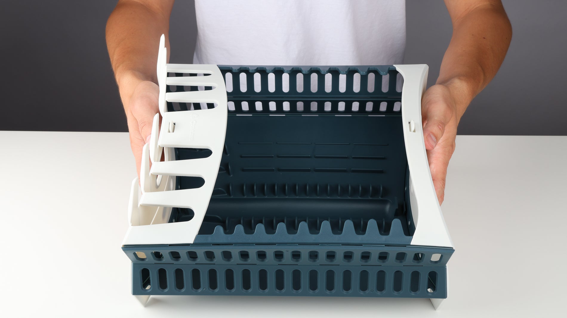 Hands holding a fully opened Coghlan's dish rack on a white table