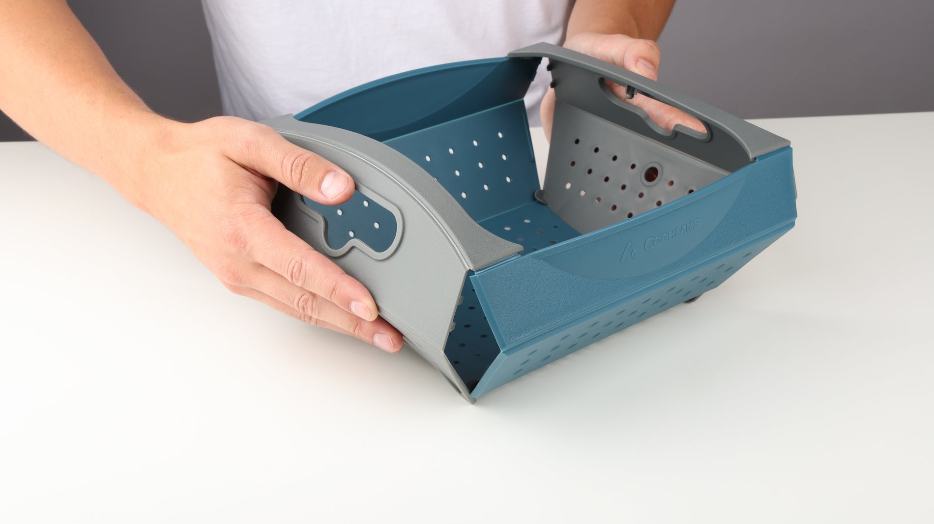 Hands pressing on the sides to lift and open up the Coghlan's Snapfold Colander