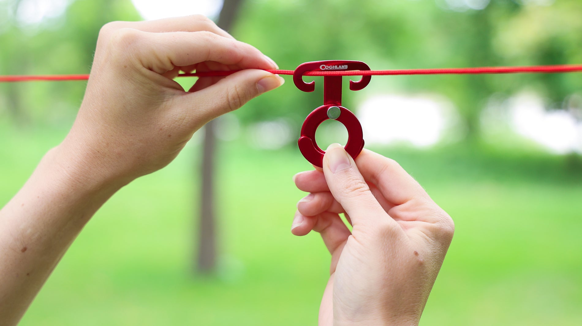 A person's hands attaching the hooks of a Coghlan's Anchor Clip on a red cord