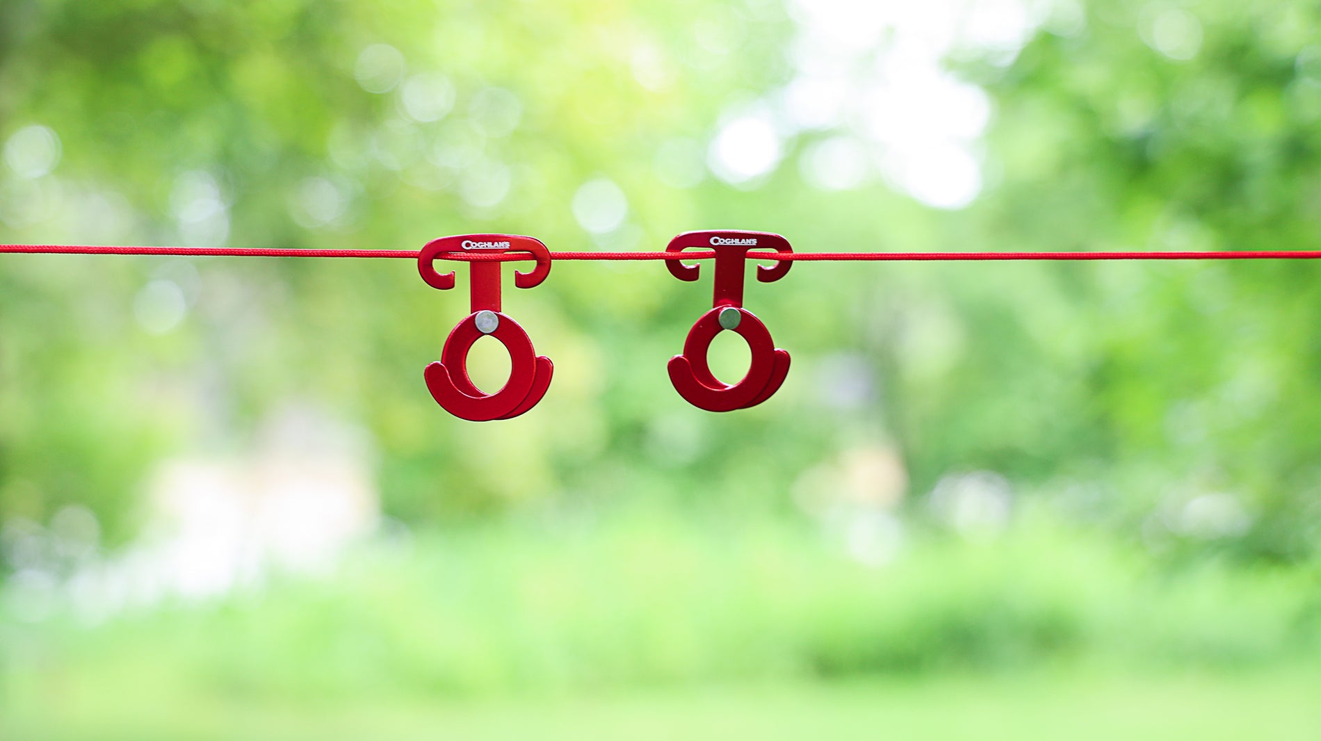 Two Coghlan's Anchor Clips attached to a hanging cord with blurred trees in the background