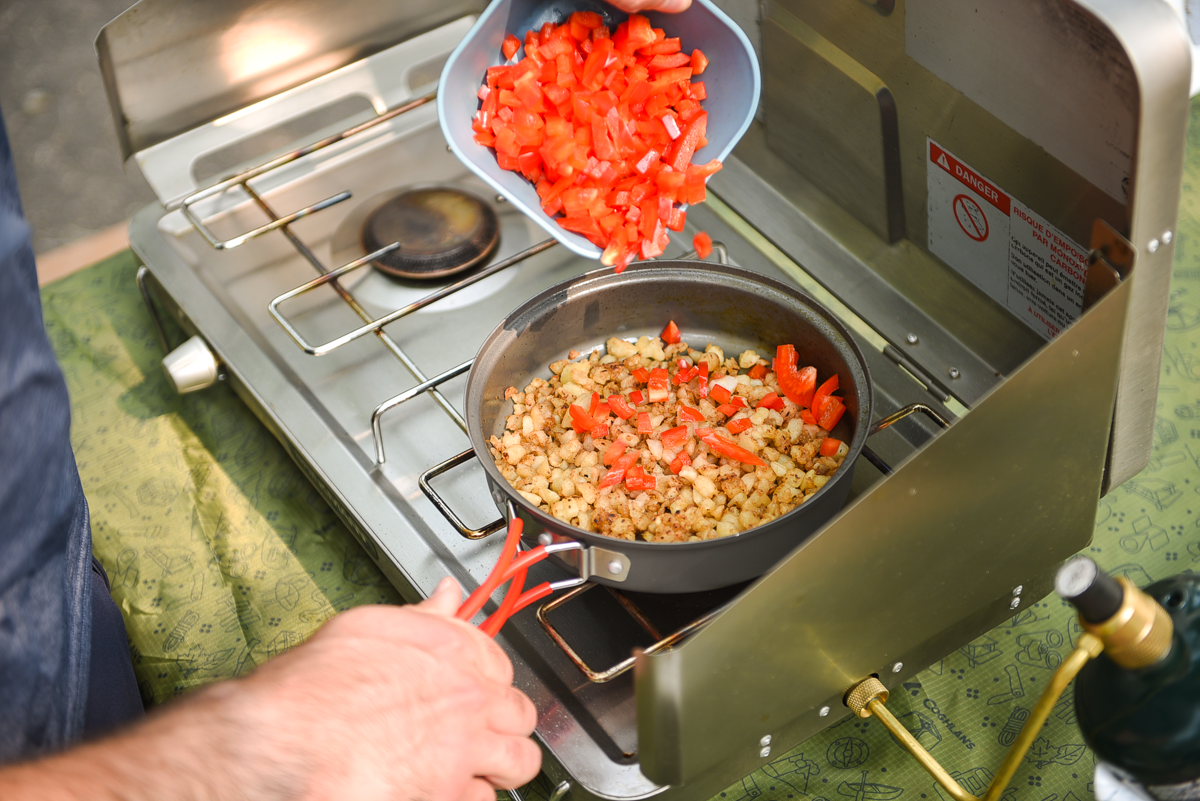 adding diced red pepper to hashbrowns in the frying pan