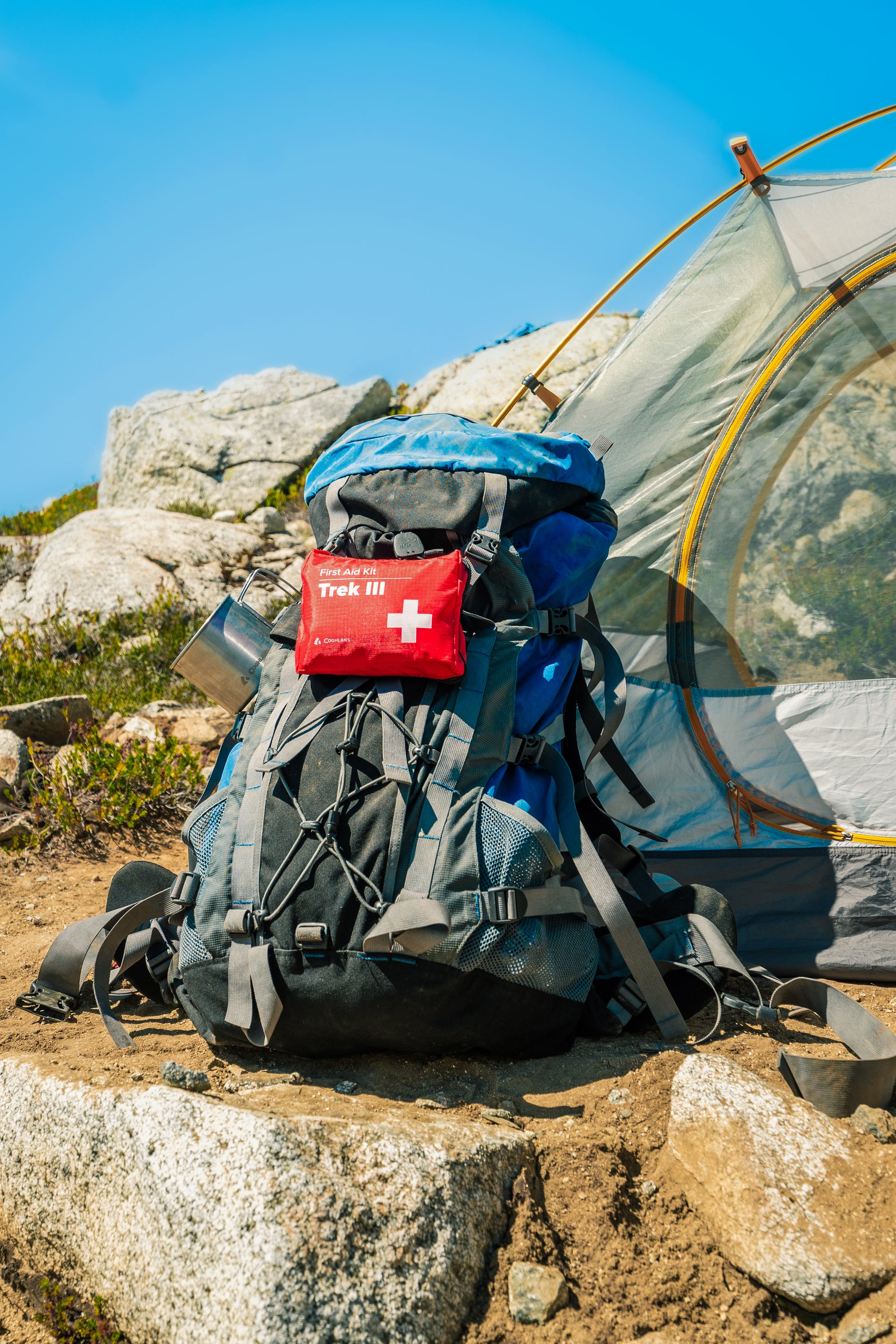 A fully-equipped hiking backpack on rocky terrain next to a lightweight tent