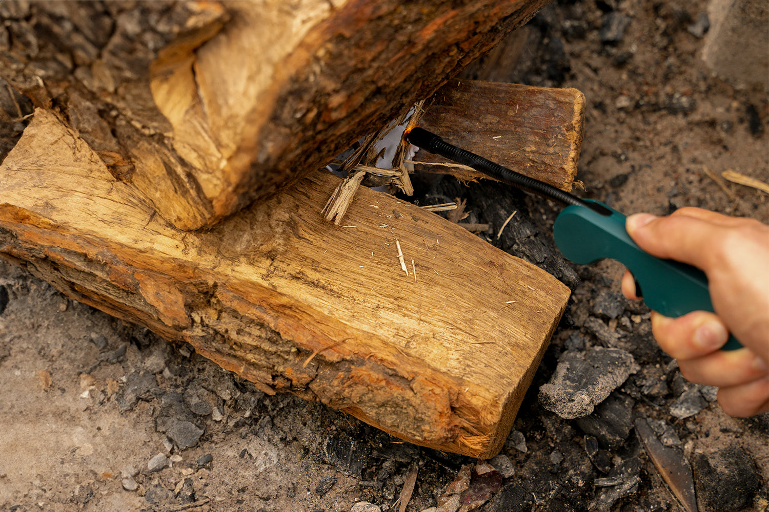 Close-up of a dark green flex lighter lighting tinder and kindling placed underneath numerous logs