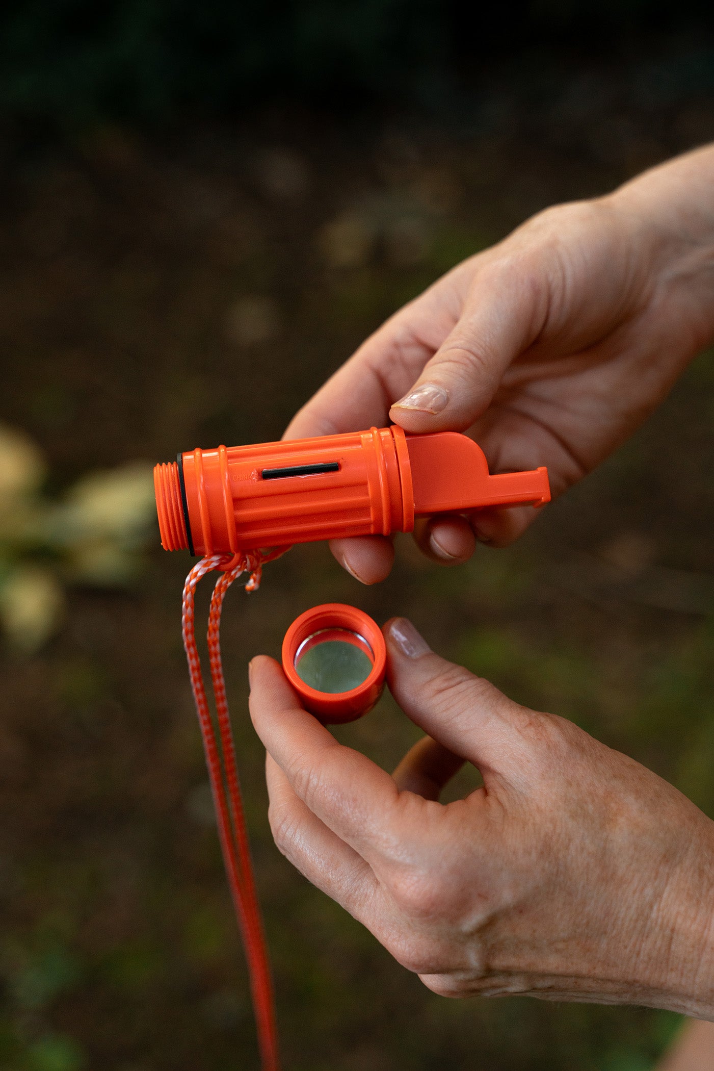 Close-up view of two hands holding an orange survival aid device in the wildnerness