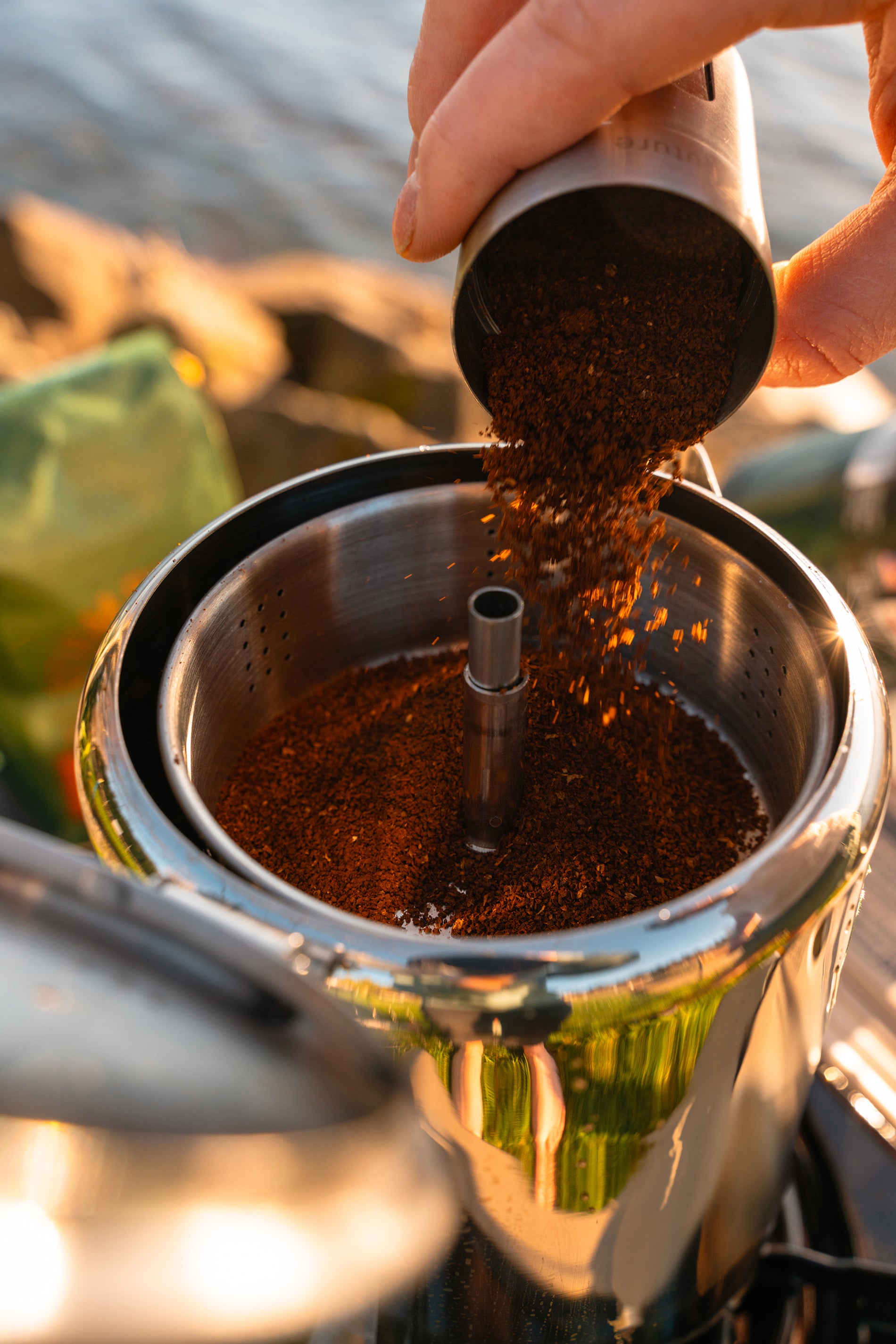 Close up image of someone pouring coffee grounds into a percolator style coffee pot