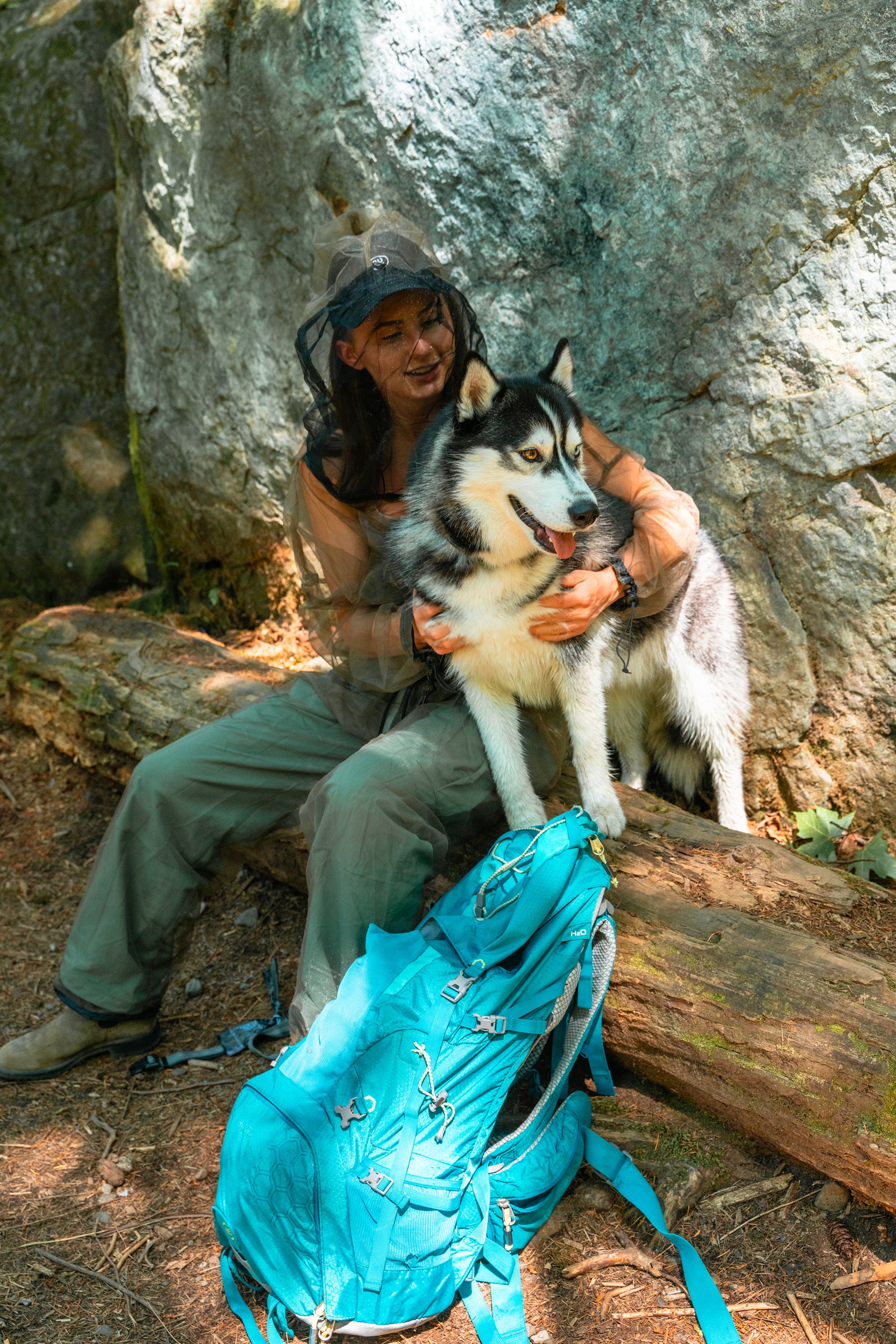 Young woman and her husky sitting on a log against a boulder in the forest