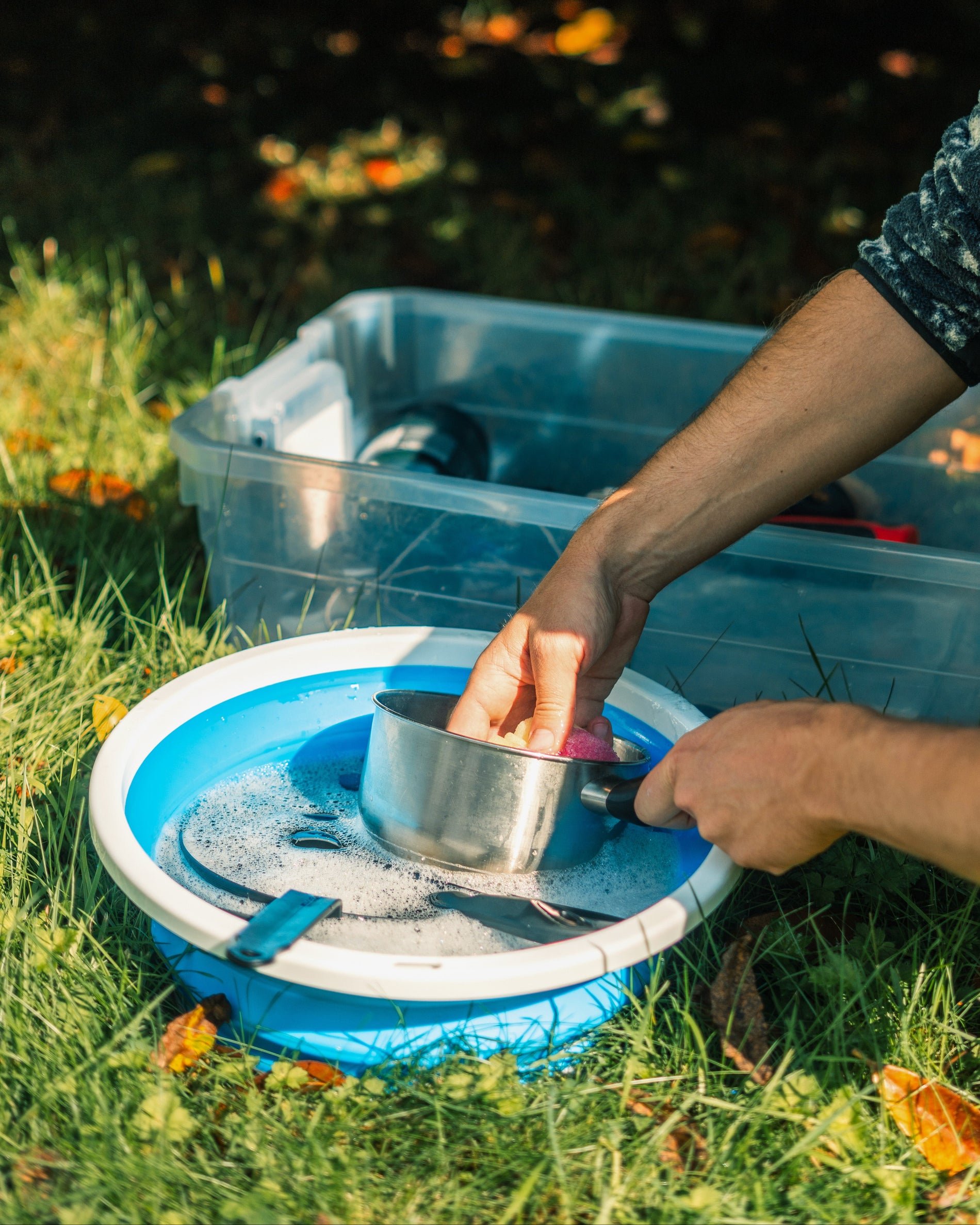 A man washing pots and pans in a collapsible sink with soapy water at a campsite