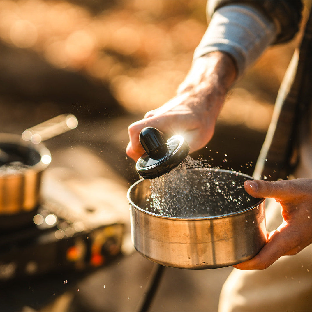 Close-up of a man washing out a lightweight pot with the spray of a portable shower