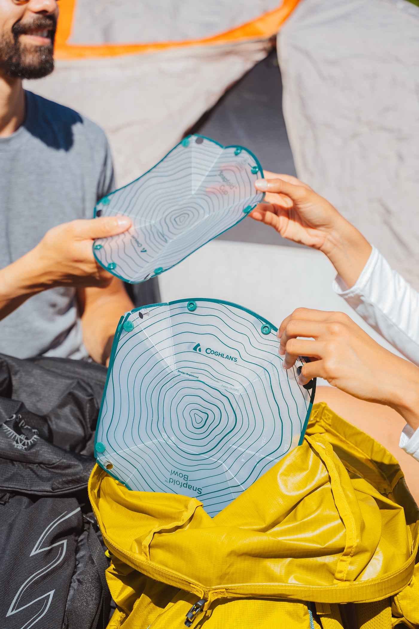 Close-up of hands pulling two pieces of collapsible dishware out of a yellow hiking backpack