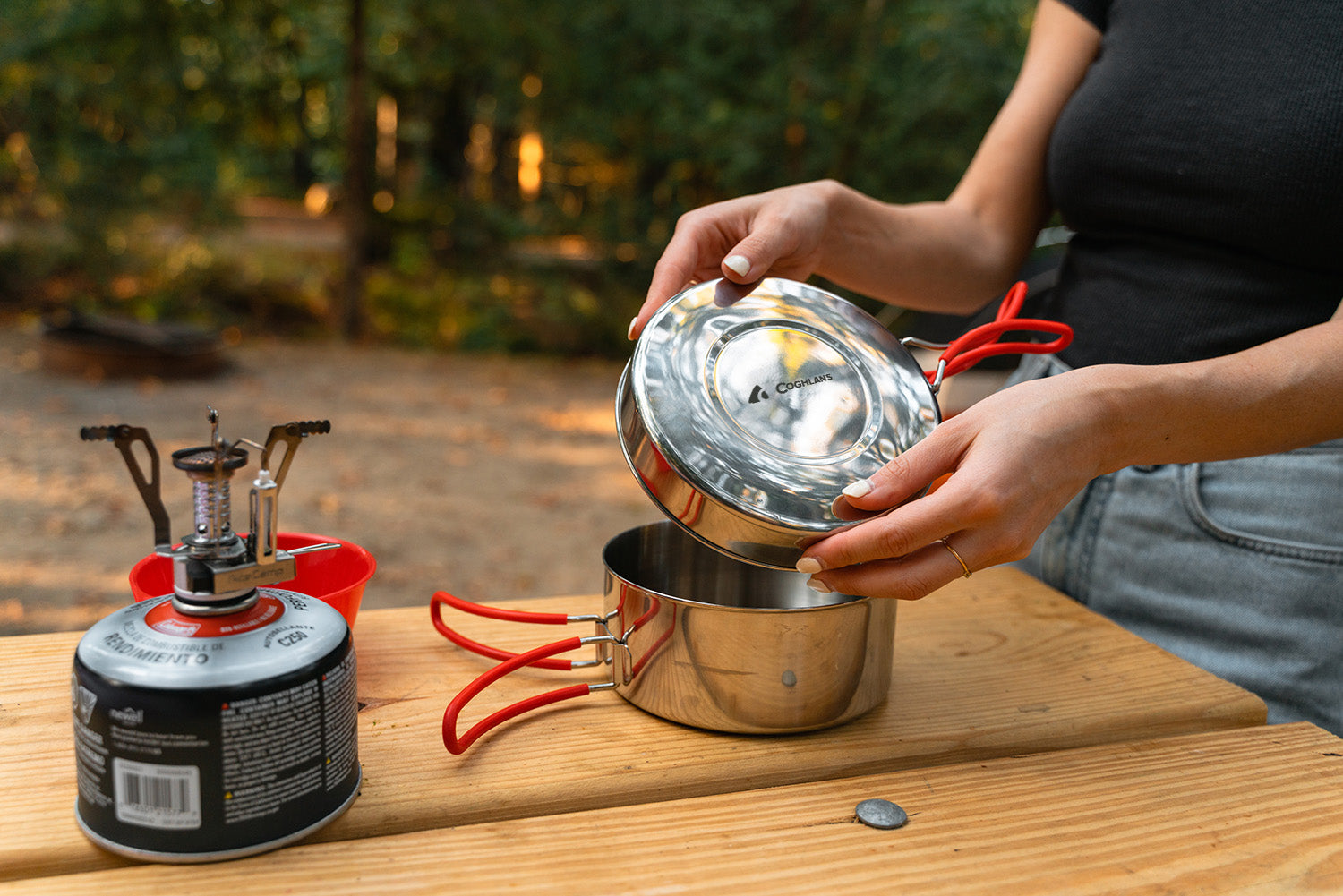 Close-up of a woman's hands packing up a stainless steel mess kit at a campsite