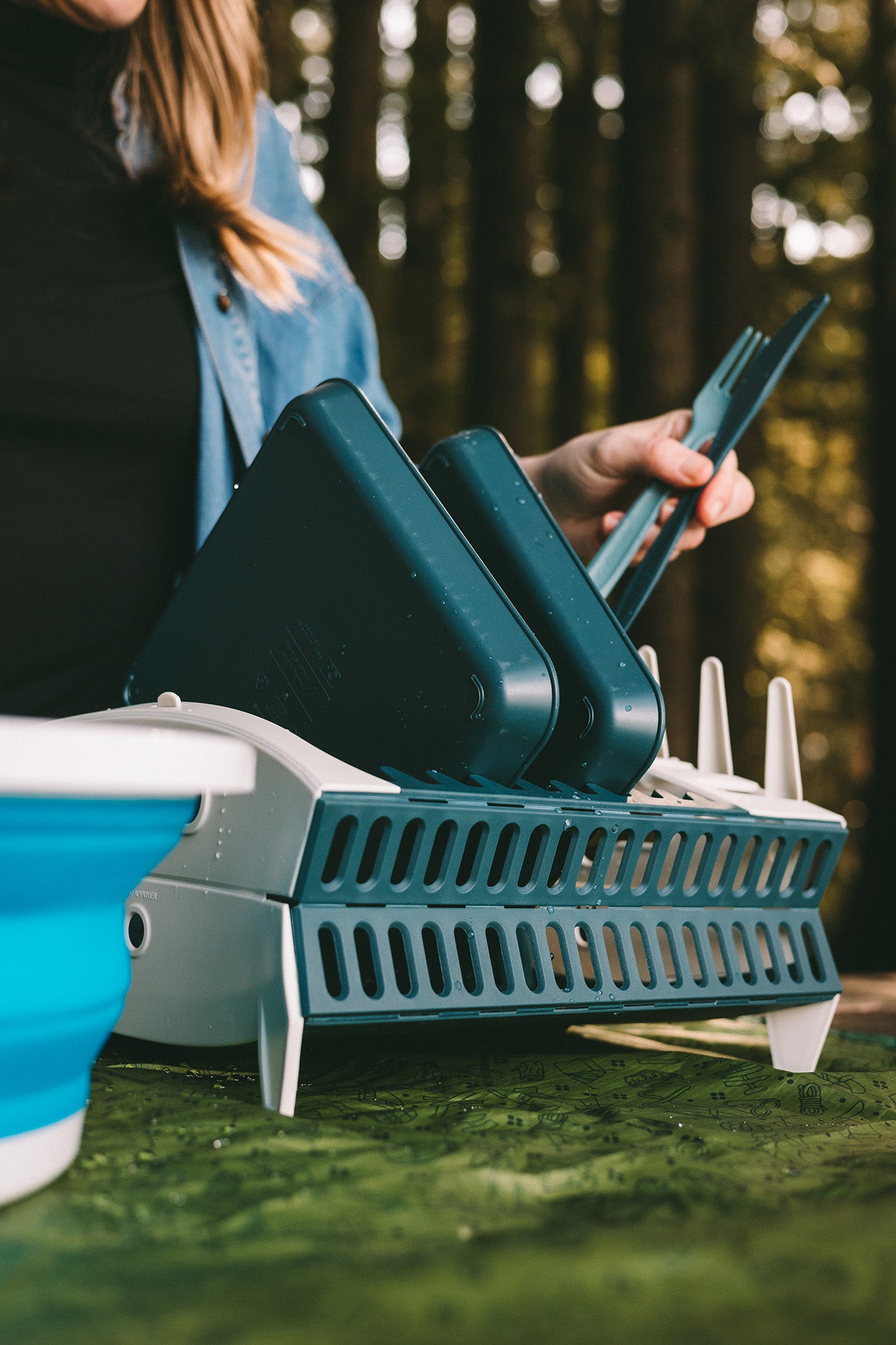 Woman placing plates and utensils in a pop-up dishrack on a picnic table
