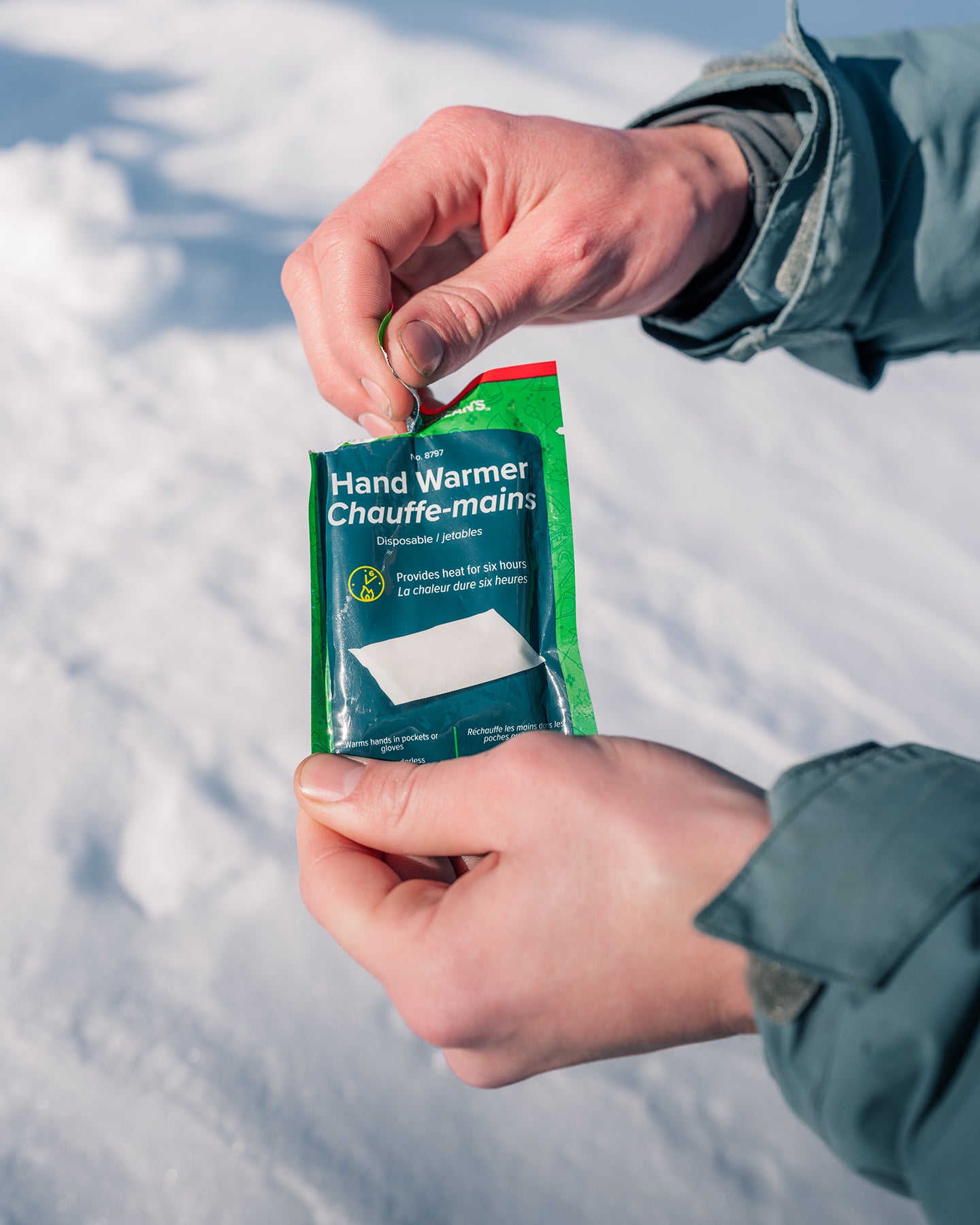 Close-up of a person opening a packet of hand warmers over a snow bank